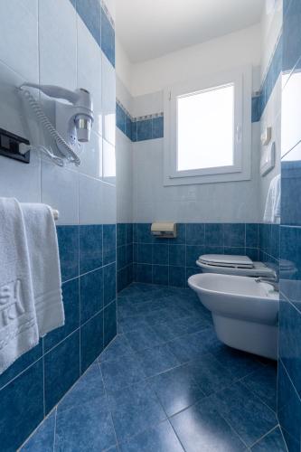 a blue tiled bathroom with a toilet and a window at Hotel Kennedy in Lido di Jesolo