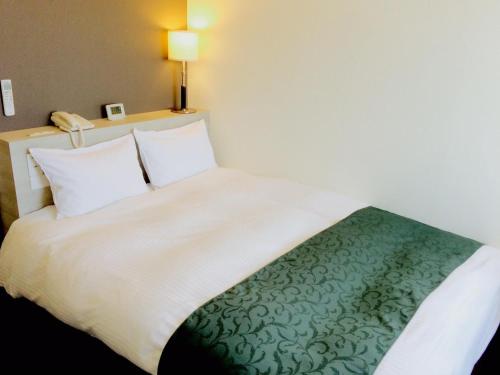 a bedroom with a white bed with a green blanket at Hotel Monteroza Ohta in Ota