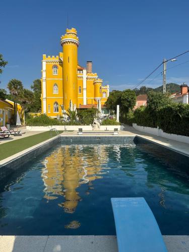 a pool in front of a yellow building with a lighthouse at Vila Aurora in Luso