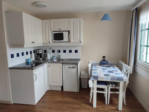 une cuisine avec des armoires blanches, une table et un micro-ondes dans l'établissement Le goéland 2 piéces avec terrasse, 4 personnes, à Talmont-Saint-Hilaire