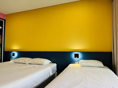 two beds in a room with a yellow wall at FLAMINGO Ibiza HaiTien - Ivy Abtel in Thanh Hóa