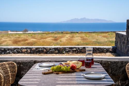 a table with a plate of fruit and two glasses of wine at Platies Luxury Apartments Santorini in Éxo Goniá
