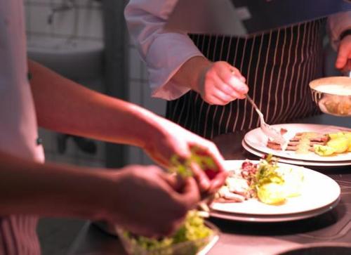 two people preparing food on a table with plates of food at Adler Hotel & Restaurant Groß-Gerau in Groß-Gerau