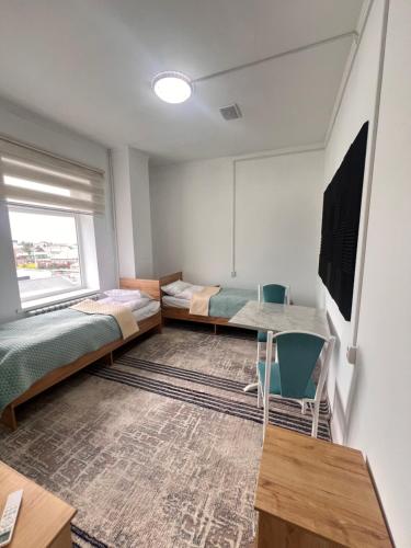 a room with two beds and a desk and a window at Sayak hostel in Karakol