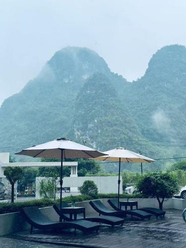 a group of tables and umbrellas in front of a mountain at Yangshuo-Greenery Retreat in Yangshuo