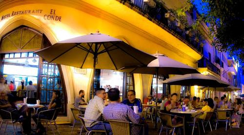 personas sentadas en mesas en un restaurante con sombrillas en Hotel Conde de Penalba en Santo Domingo