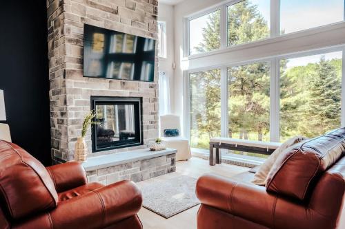 a living room with two leather chairs and a fireplace at Modern Waterfront Cottage on the Rouge River & Spa in Rivière-Rouge