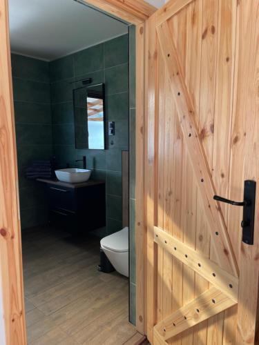 a bathroom with a wooden door with a toilet and a sink at Domek Na Miodowej in Sulistrowiczki