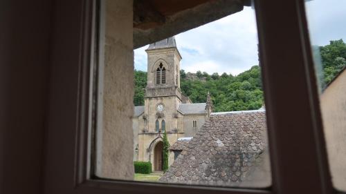 a view of a church with a clock tower from a window at La Maison du Griffoul BB à Salles la Source cascade et terroir in Salles-la-Source