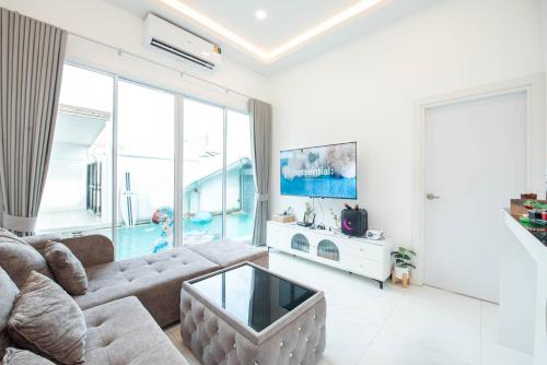 a living room with a couch and a tv at Mina Pool Villa in Ban Huai Yai