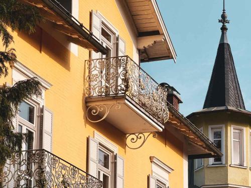 a yellow building with a balcony and a steeple at Villa Dora Petit Hôtel in Bad Reichenhall