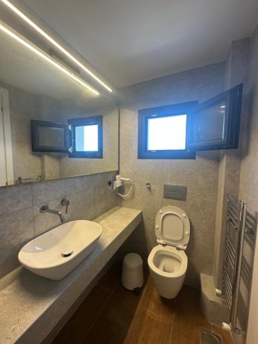a bathroom with a sink and a toilet and two windows at Mare Beach Apartments in Stavros