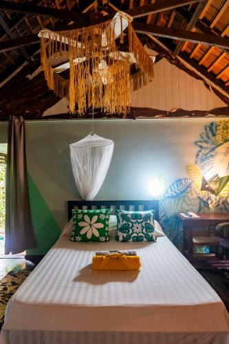 a bed with green and white pillows and a chandelier at Fare Club Moorea in Motu Tiahura