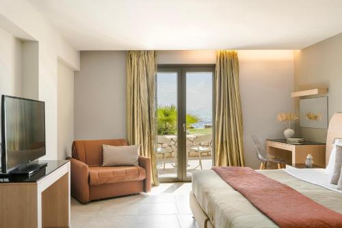 a hotel room with a bed and a television and a chair at Alas Resort & Spa in Elia Laconias