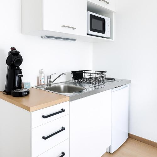 une cuisine blanche avec un évier et un micro-ondes dans l'établissement Le Cocon - Vue panoramique Strasbourg - Wifi - Netflix, à Strasbourg
