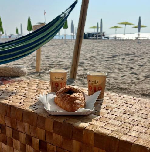 a table with a plate of pastries and two drinks on the beach at Camping Grande Italia in Chioggia