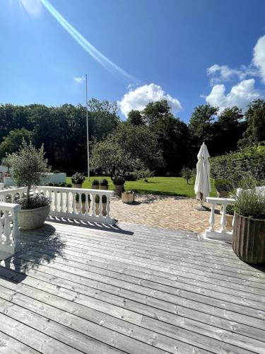 a wooden deck with white benches and an umbrella at Large pool villa close to forest in Risskov
