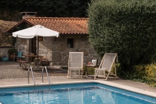 a swimming pool with two chairs and an umbrella at Casa da Janeira in Vieira do Minho