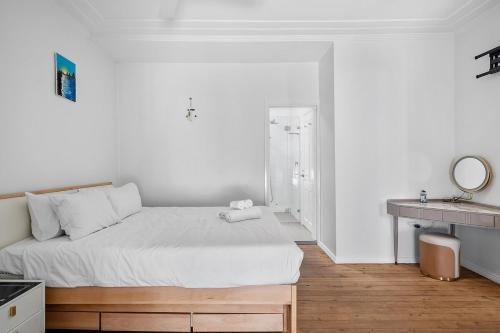 a white bedroom with a bed and a mirror at Poolside 3BR Coastal Retreat in Avalon Beach in Whale Beach