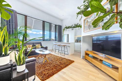 a living room with a large tv and some plants at Waterfront Loft at Quay, Walk to Ferry & Train in Auckland