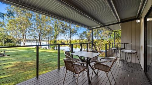 a screened porch with tables and chairs and a view of a field at Wooli River Lodges in Wooli
