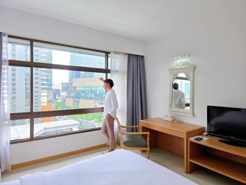 a man standing in a hotel room looking out the window at Pinnacle Lumpinee Park Hotel in Bangkok
