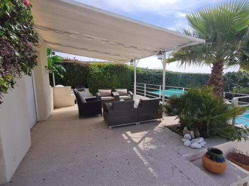 un patio avec des canapés et un auvent avec une piscine dans l'établissement Villa 5 pièces + 2 chambres indépendantes - Piscine privée, jardin, climatisation, Wi-Fi - FR-1-780-79, à Grimaud