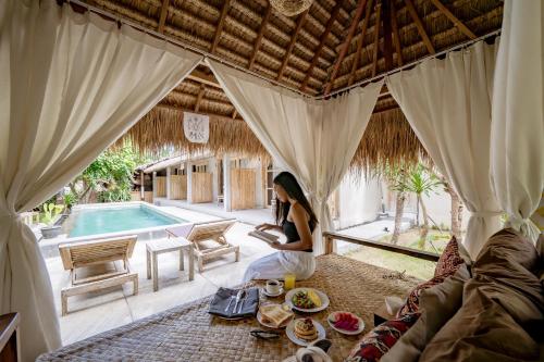 a woman sitting on a couch in a room with a pool at Golden Garuda Cottages at Diamond Beach Hills in Nusa Penida