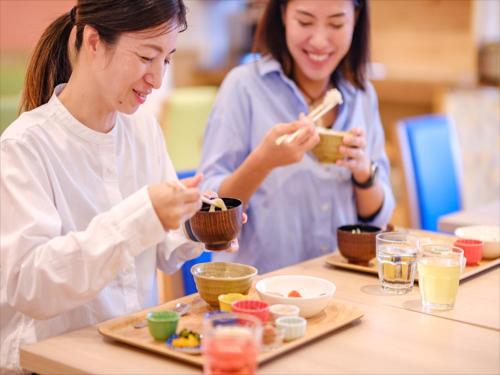 two women standing at a table eating food with chopsticks at Hotel Risingsun Miyakojima in Miyako Island