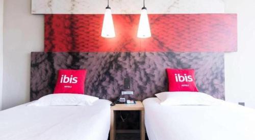 two beds in a room with red pillows on them at Ibis Nantong Qingnian in Nantong
