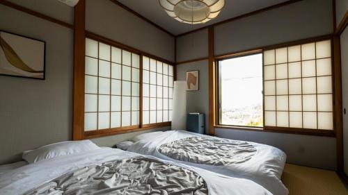 a bedroom with two beds and two windows at マイグレフラット in Ito