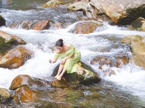 a woman in a dress sitting on a rock in a river at Bamboo Home in Sa Pa