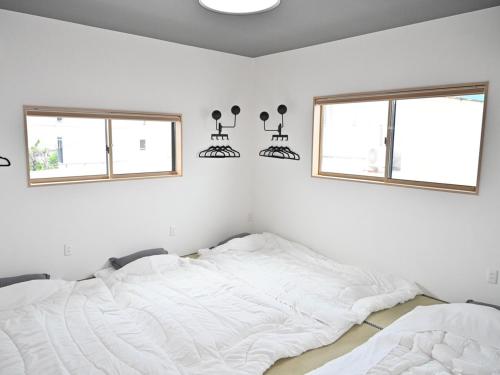 a white bedroom with two beds and two windows at ｹﾞｽﾄﾊｳｽ ﾊﾞｲｸﾔﾉﾆｶｲ in Hagi