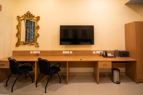 a desk with two chairs and a television on a wall at Mayfair World Cup Village in Rourkela
