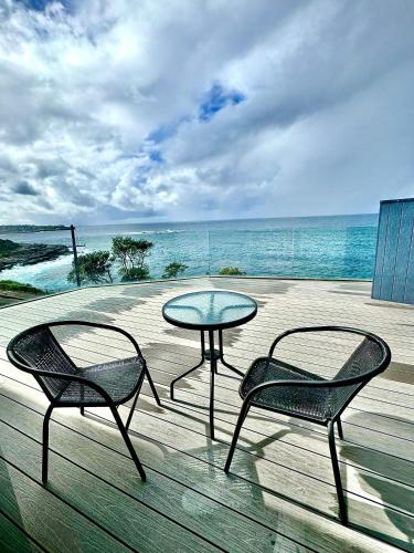 two chairs and a glass table on a deck with the ocean at Ocean view home South Coogee in Sydney
