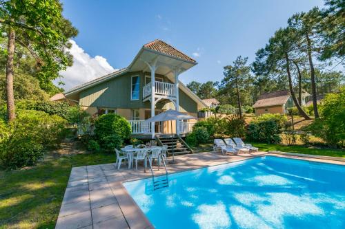 une maison avec une piscine devant une maison dans l'établissement Lagrange Vacances - Eden Club, à Lacanau-Océan
