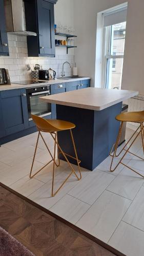 a kitchen with blue cabinets and a counter with two chairs at 1A Cathedral Place - Cathedral Townhouses Cobh in Cobh