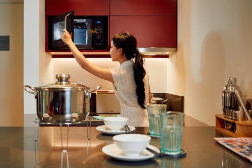 a woman standing in a kitchen reaching for a microwave at Wink Icon Hotel Danang Riverside - 24hrs Stay & Rooftop Pool Bar in Da Nang