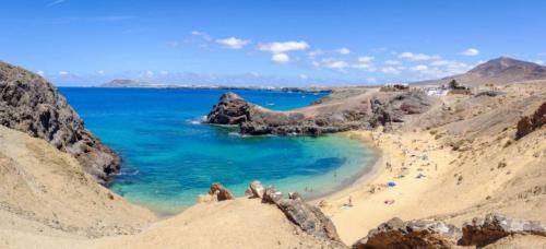 a beach with people in the sand and blue water at Apartamentos y Lofts Makana in Playa Blanca