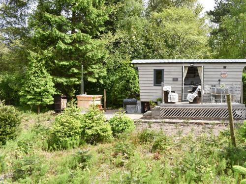 a small white shed with a porch and two chairs at Spruce Shepherd's Hut in Wilmslow