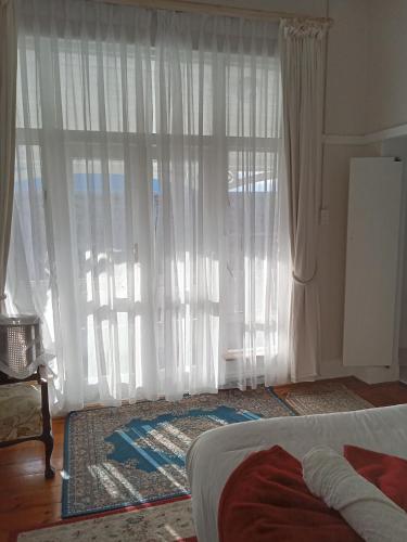a bedroom with a large window with white curtains at Kardinal guesthouse on 44 St Phillips street in Gqeberha