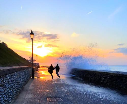 two people walking on a beach with a wave at Huge 6 Bedroom House in Sheringham in Sheringham