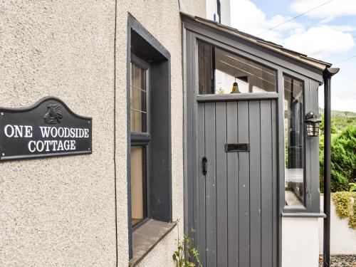 a building with a grey door and a one wonders cottage sign at Wood-Side Cottage in Backbarrow
