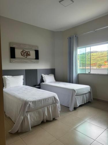 two beds in a white room with a window at Hotel Yoguedes in Padre Paraíso