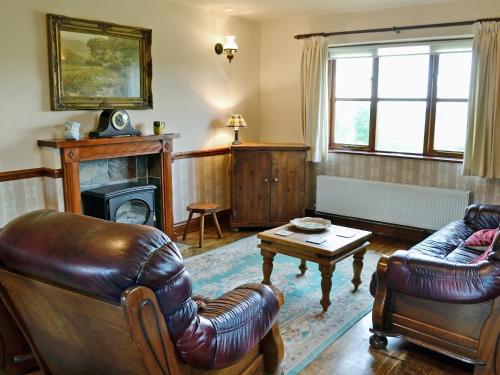 Elle comprend un salon doté d'un mobilier en cuir et d'une cheminée. dans l'établissement Woods Cottage, à Evershot