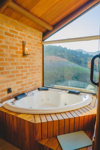 a bath tub in a room with a large window at Pousada Ho'oponopono Chalets & Wine in Sapucaí-Mirim