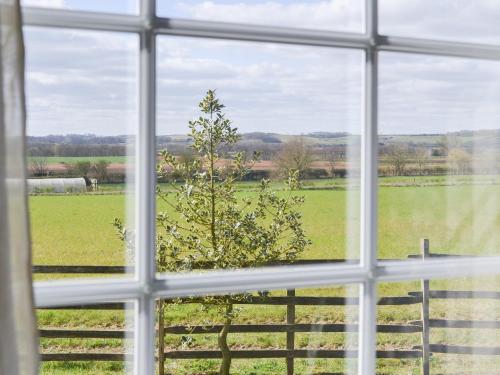 a window with a view of a field and a tree at The Shepherds Bothy in Tetford