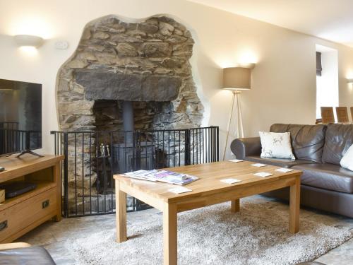 a living room with a table and a stone fireplace at Wood-Side Cottage in Backbarrow