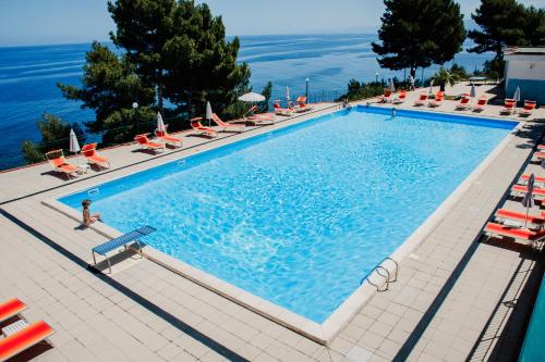 a large swimming pool with lounge chairs and the ocean at Camping & Village Rais Gerbi in Pollina