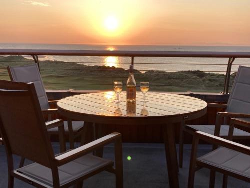 a table with two wine glasses on a balcony with the sunset at Penthouse Golf View Apartments in Lossiemouth